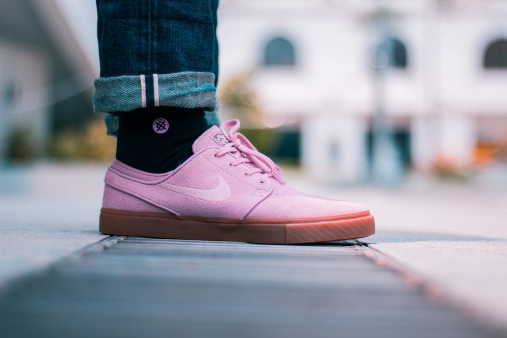 Close-up of pink sneakers worn with rolled-up jeans on a city street. Fashion and style in an urban setting.
