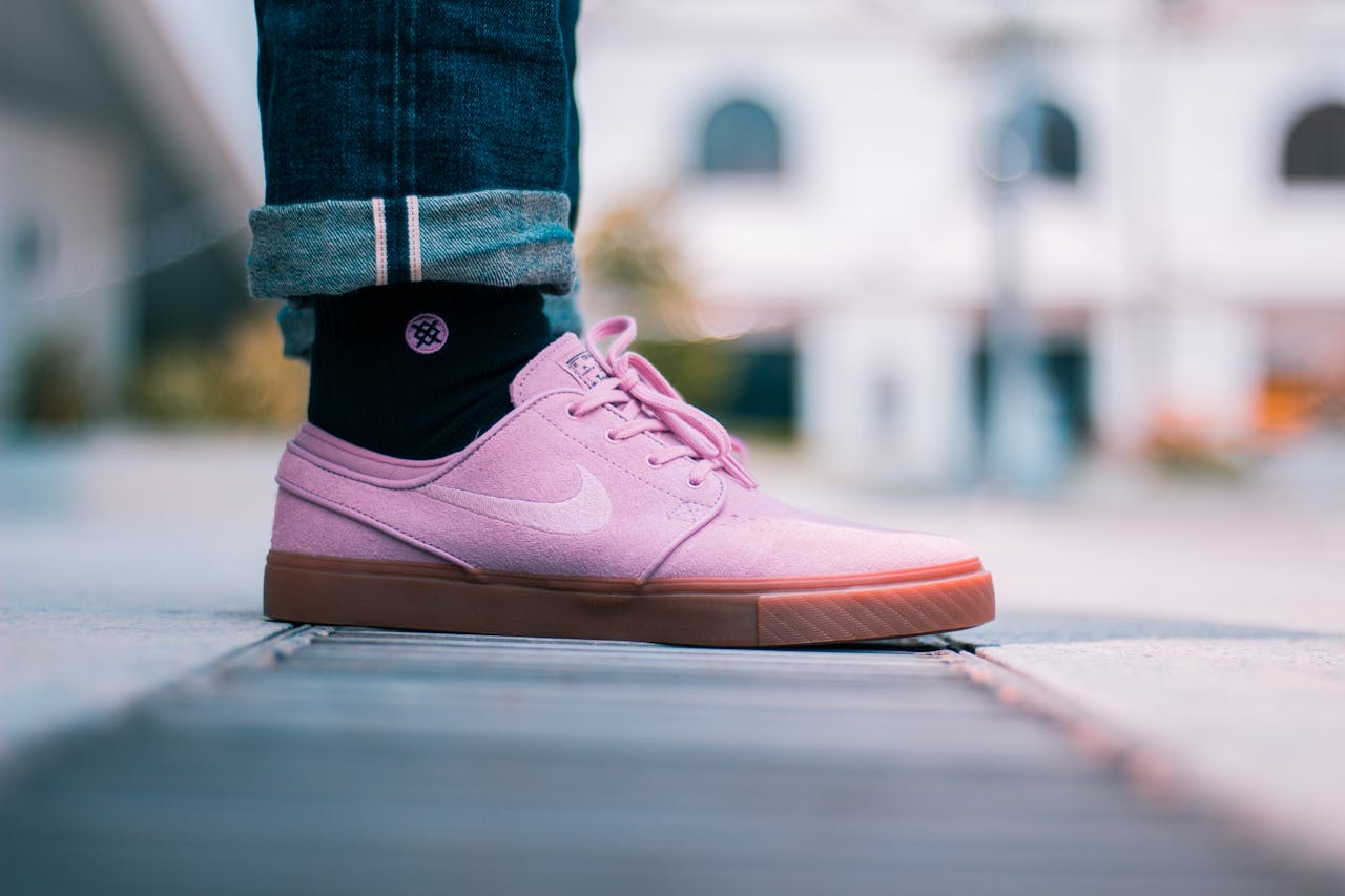 Close-up of pink sneakers worn with rolled-up jeans on a city street. Fashion and style in an urban setting.